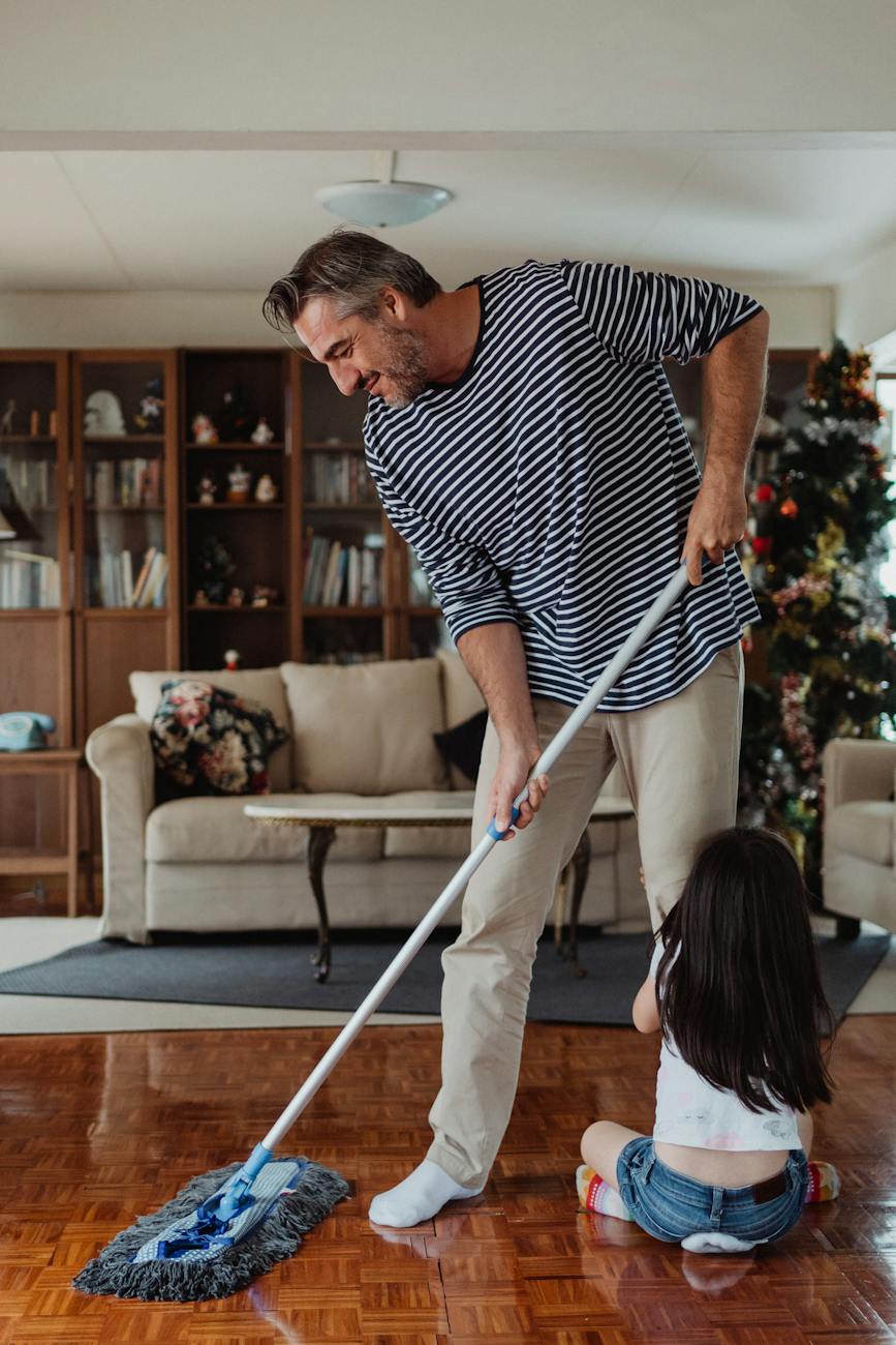 father doing chores with his daughter holding his leg