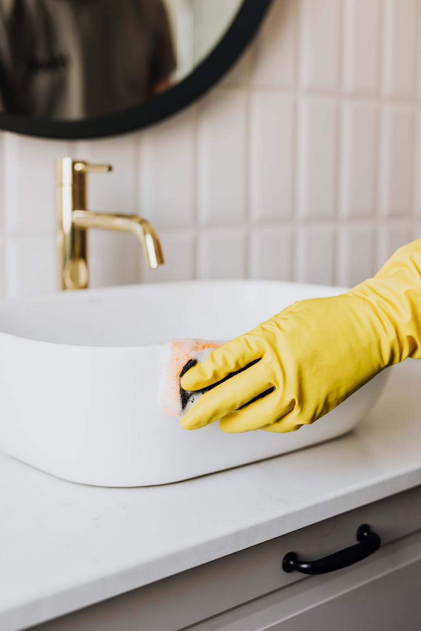 person in glove wiping surface of sink in bathroom