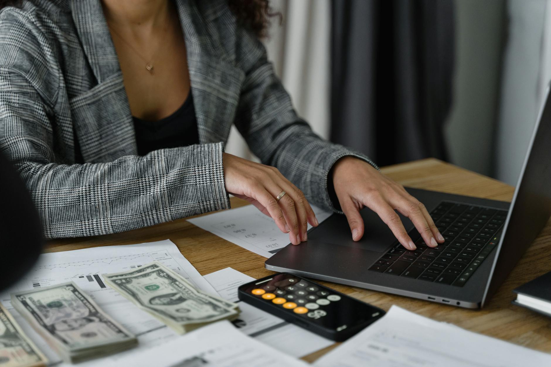 a woman using her laptop to balance her budget. There are papers and money beside her. 