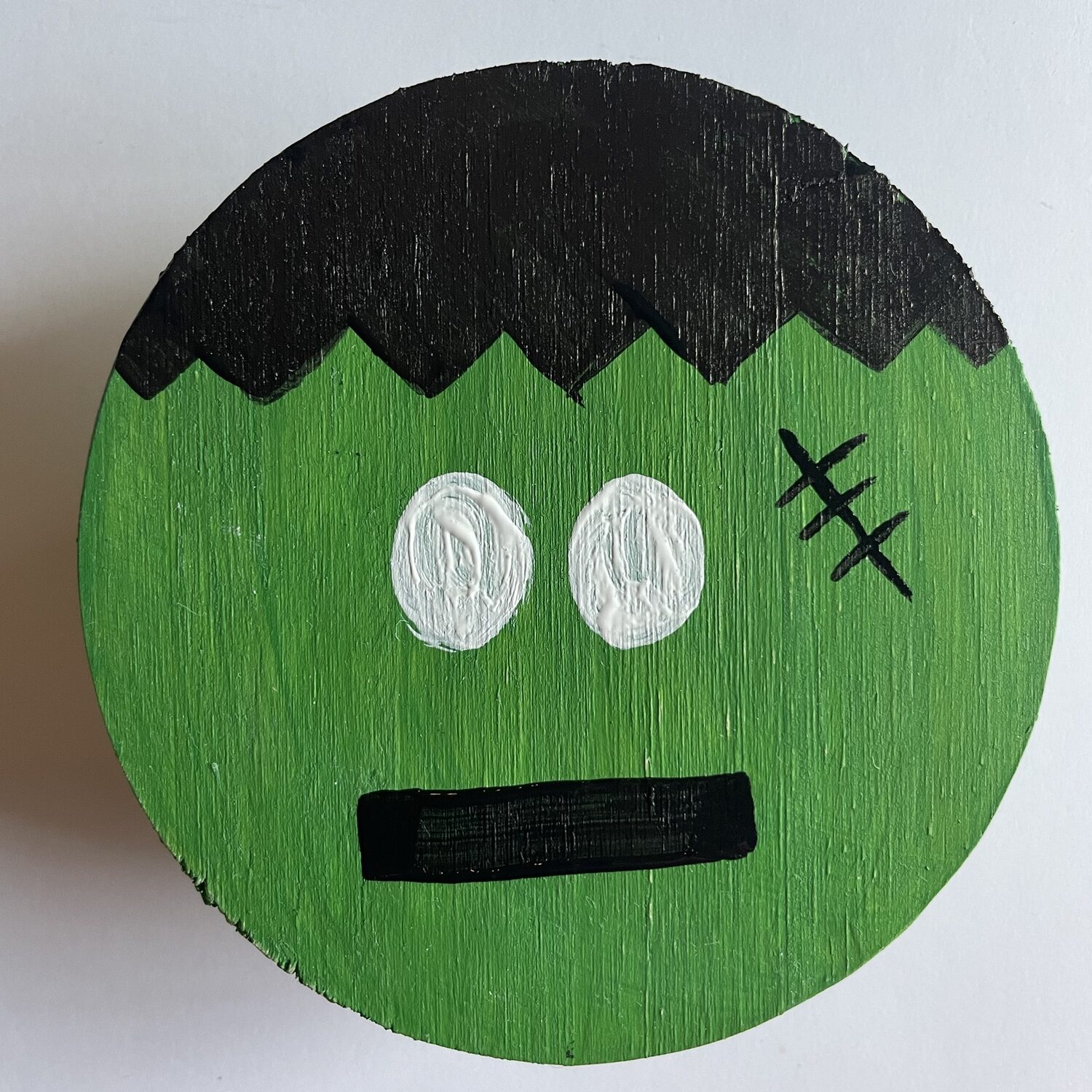 Frankenstein coaster without the pupils drawn in.  There is black hair, a black mouth, a black scar, and two white eyes. 