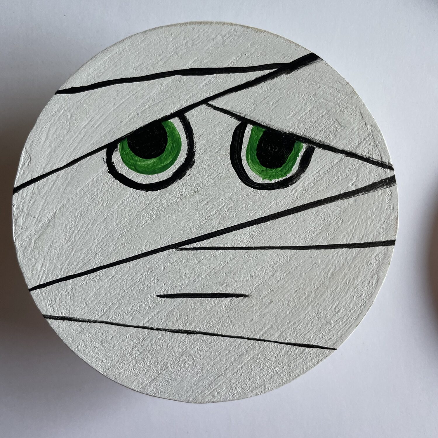 A painted mummy coaster with green eyes. 