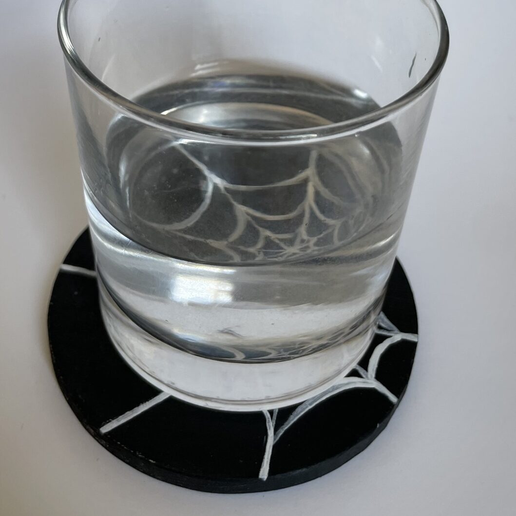 A glass of water on the spider web coaster. 