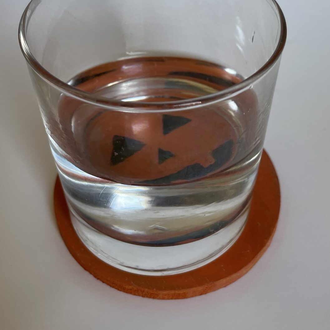 A glass of water on the pumpkin coaster. 