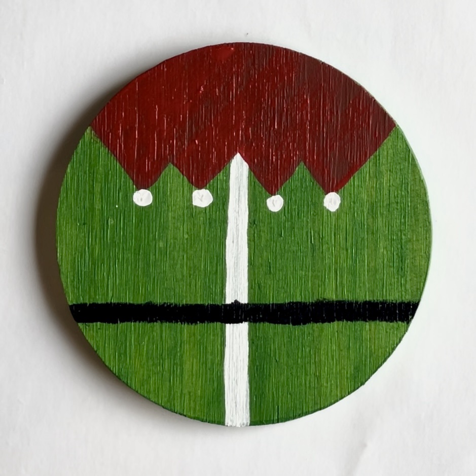Green coaster with red elf collar with white balls added to the points and a white and black intersecting line. 