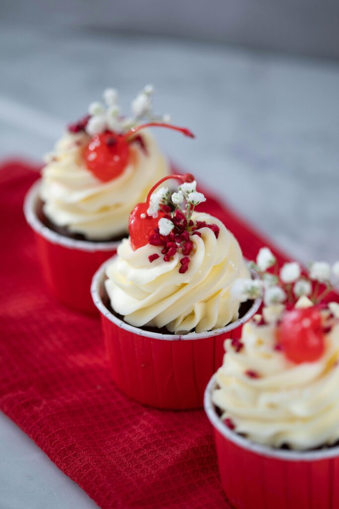 Cupcakes with red paper cups, vanilla topped with cherry and dye free red sprinkles.