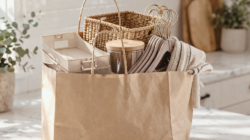A paper shopping bags with home organization objects coming out of it: hangers, baskets, etc.